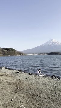 Peaceful Fuji mountain lake landscape travel nature couple view scenic water serene snowy peak rural Japan vertical footage captures happy Asian boy sitting beside calm bright sunny outdoor shore