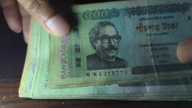 Bangladeshi currency pile counting motion footage showing stack of money banknotes with portrait of Sheikh Mujibur Rahman on wooden desk.