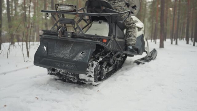 White rider on tracked ATV racing through pine forest, camouflage gear spraying snow, heavy rear track carving deep groove in winter trail, red ATV parked in distance, offroad guide and hunter persona