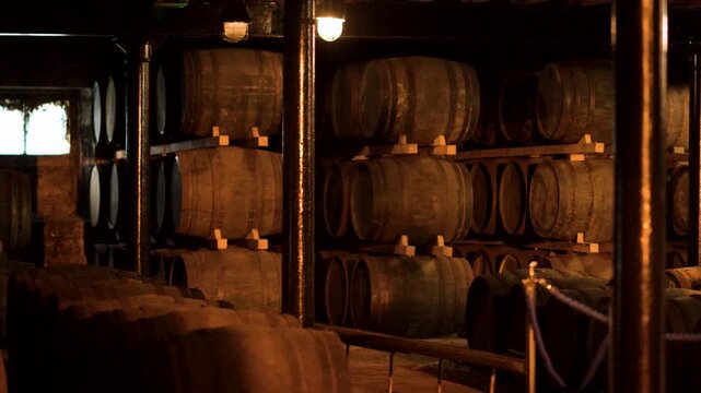 Aging wine barrels stacked in dark cellar atmospheric storage for maturation.