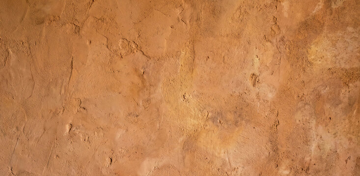 A textured surface of natural clay plaster, showcasing earthy tones and subtle variations. Suitable as a background for various design applications.
