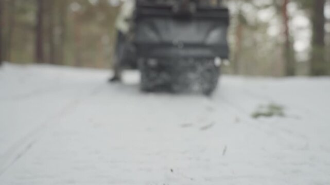 Atv rear kicking up fresh snow, close rear perspective of track spray and compact trail camoclad rider with helmet signaling and scanning forest route, steady pace through pine trees, controlled