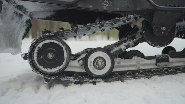 Atv track spins through packed snow, dynamic closeup of rollers and drive sprocket biting powder, ice buildup and snow spray, fast rotation showing torque and power, pine forest backdrop, gritty