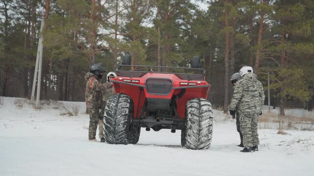 Red atv parked in snowy forest crew inspecting tires and winch, guide pointing at trail, rider mounting for offroad expedition, gear adjustment, cautionary conversation, anticipation before extreme