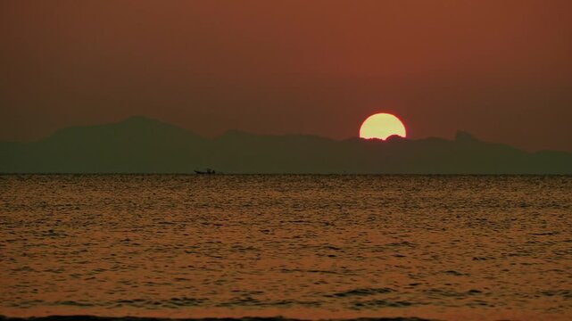 Half sun behind the remote island during tropical sunset. Koh Samui. Thailand.