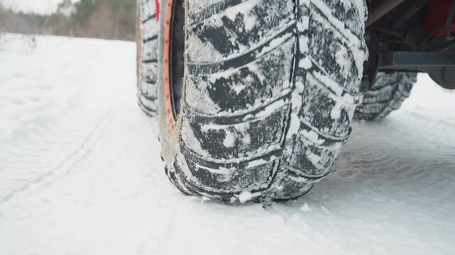 Atv wheel kicking snow closeup with orange rim flinging powder, tire tread spinning and sending snow spray, low camera angle captures acceleration and torque, pine field backdrop, fastpaced adrenaline