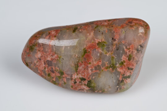 Smooth unakite pebble displaying lively mineral colors on plain surface. Polished unakite gemstone characterized by vibrant mineral inclusions against neutral backdrop