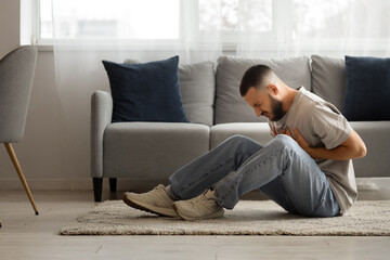 Fototapeta premium Depressed young man sitting on carpet at home. International Stress Awareness Week