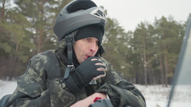 Rider ready on snowmobile, blowing vapor and scanning trail ahead in winter pine forest helmeted man grips handlebars, focused expression, engine noise implied, snow and powder around windshield,