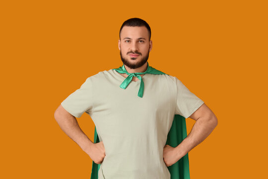 Young man with superhero cape on orange background