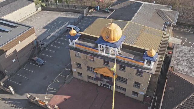 Guru Nanak Gurdwara Sikh temple on Halifax Old Road Huddersfield Kirklees West Yorkshire England United Kingdom with golden domes and Nishan Sahib flag, drone orbit shot