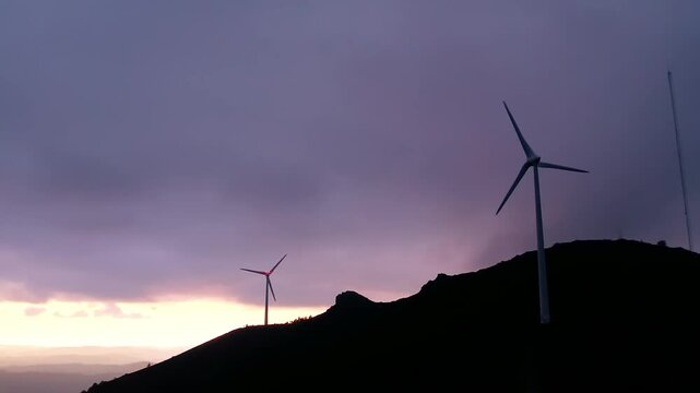 Nordex three blade wind turbines standing as silhouettes on a mountain ridge at Serra da Boneca, capturing wind energy during dusk to produce renewable electricity, symbolizing environmental progress