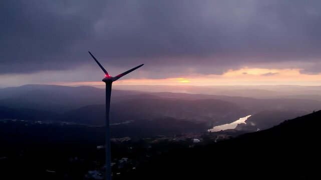 Wind turbine horizontal axis type on Serra da Boneca ridge in Centro region Portugal over Mondego River valley at sunset with steady wind conditions and aviation light, drone slow push