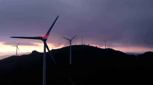 Wind turbines generating clean energy at Serra da Boneca wind farm in Portugal, silhouetted against a vibrant sunset sky, symbolizing sustainable power and future green technology development panning