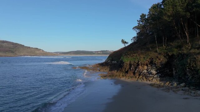 Secluded Sandy Beach Praia das Vacas In Galicia, Spain, With Waves Splashing On Rocky Coastline. sideways drone shot