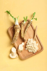 Fototapeta premium Wooden board with horseradish sauce, roots, slices and spoon on yellow background
