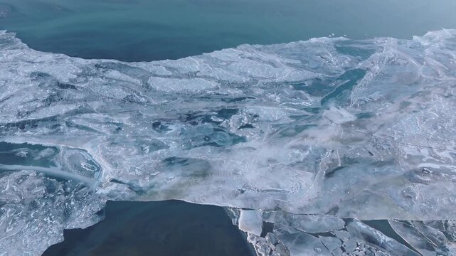 Stunning aerial footage of glacial ice sheets merging with deep blue ocean water along the South Iceland coastline. Abstract frozen textures and swirling ice patterns create a breathtaking natural sce