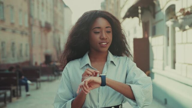 Woman uses smartwatch, Urban woman in striped shirt swiftly responds to notification with focused concentration