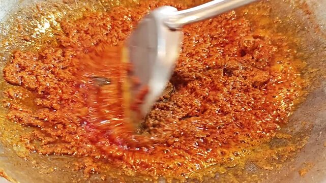 Close up of stirring spicy red curry paste in a wok to release aromatic flavors.