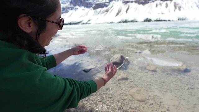 Woman's hands holding a thin sheet of ice from the partially frozen Bow Lake in Banff National Park