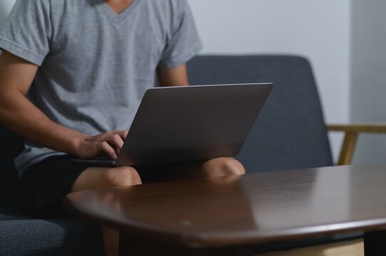 Relaxed person using laptop on sofa with wooden coffee table