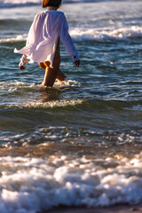 Fototapeta premium Summer mood. A slender girl walks along a sandy beach. Close-up of her legs. The woman enjoys.