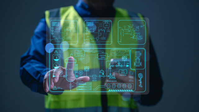 Industrial engineer wearing safety vest monitors automated factory plant control system hologram interface. Professional technician manages manufacturing data analytics dashboard futuristic digital