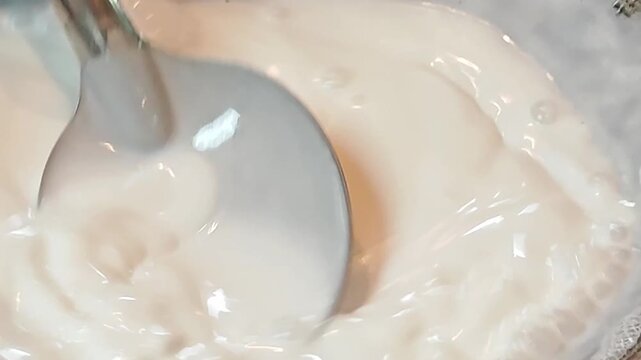 Close up of fresh creamy coconut milk being stirred with a spoon in a pot.