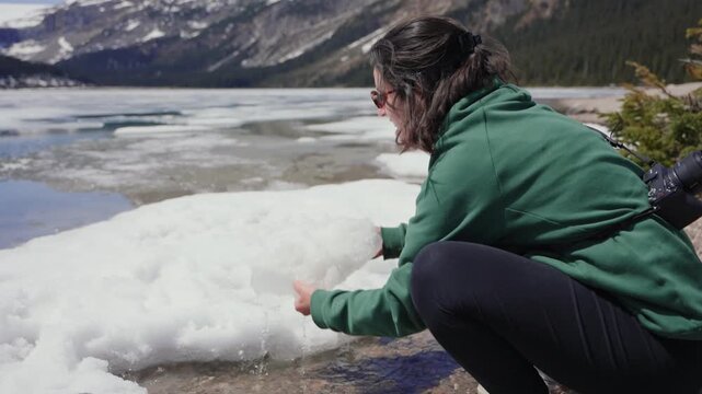 Woman feeling cold while holding a large ice block outdoors in a snowy mountain lake