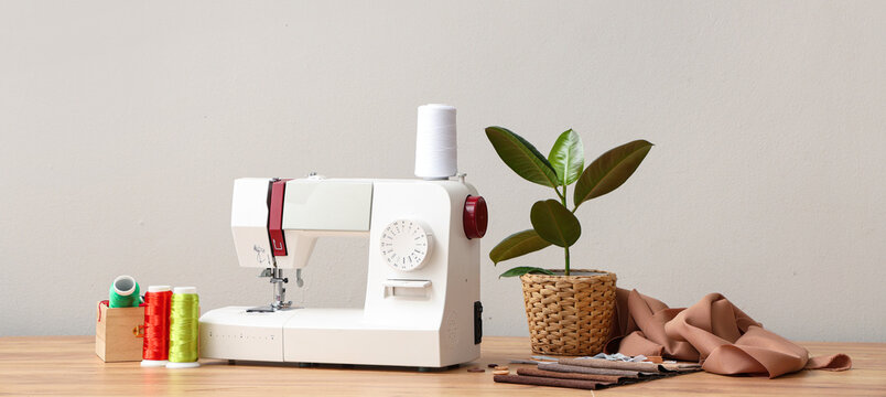 Modern sewing machine with tailor's supplies on wooden table