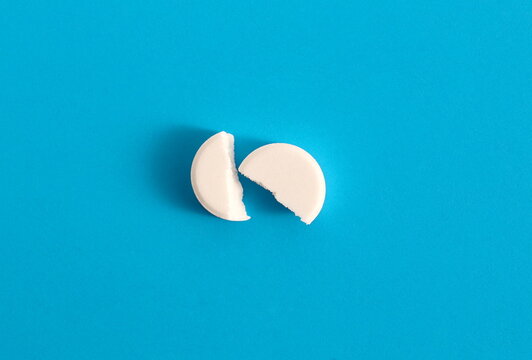 On a blue background lies a white medicine tablet broken in half.