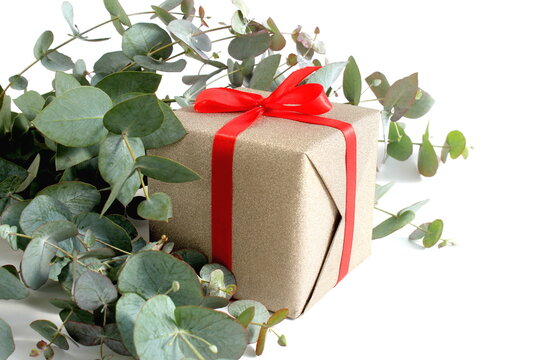 On a white background lie eucalyptus branches with a gift box with a red bow.