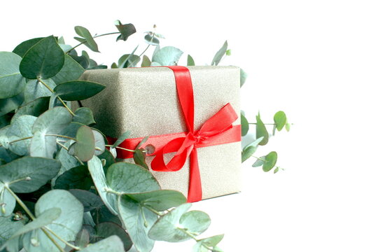 On a white background lie eucalyptus branches with a gift box with a red bow.