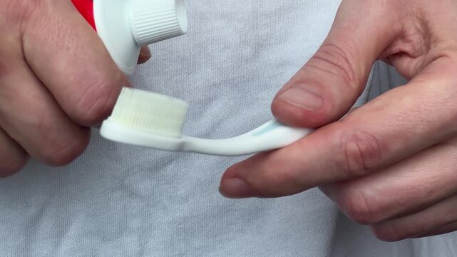 Close up of adult hands holding white toothbrush and toothpaste tube, before applying paste for daily dental care
