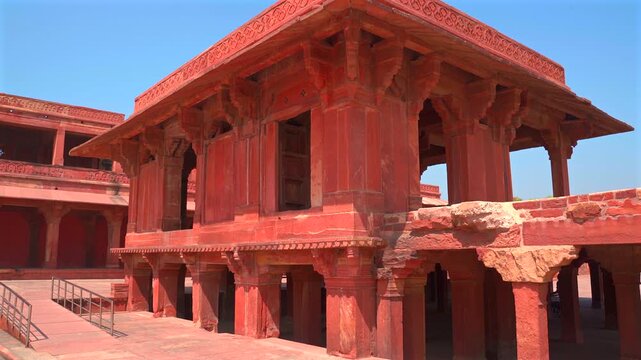 A static low-angle shot of a traditional red sandstone pavilion with ornate pillars and carved cornices, located within the UNESCO World Heritage site of Fatehpur Sikri.