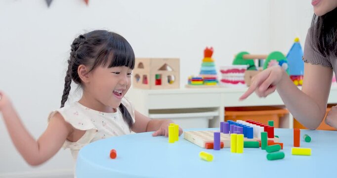 Asian single mother assisting preschool daughter placing colorful rods onto learning board, close home development activity boosting counting skill, fine motor practice, logic, supportive family bond