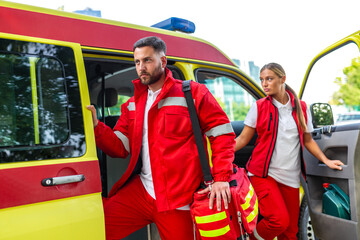 Professional male and female paramedics in red uniforms getting out of an ambulance with a medical bag. Emergency medical team arriving at a rescue scene. Healthcare and first responder concept. © Graphicroyalty