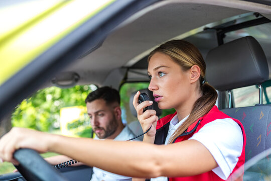 Young female paramedic using a handheld radio transmitter while sitting in the driver seat of an ambulance. Professional emergency medical team responding to an urgent call. Healthcare background.