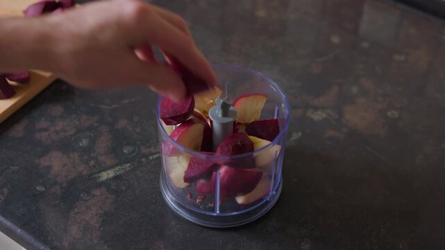 Static tripod shot of a person putting beetroot slices into a blender bowl with apples