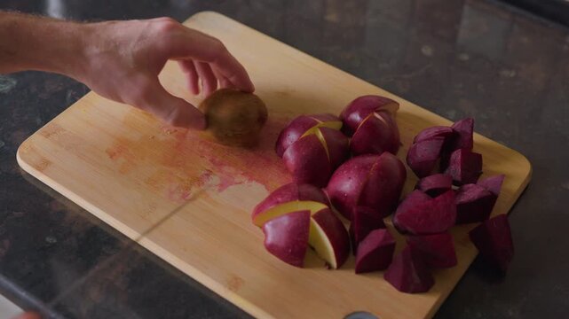 Static tripod shot of a man slicing kiwi on a wooden board with apples and beets