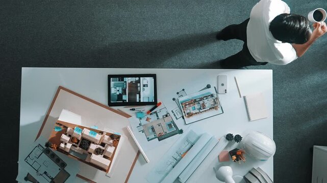 Top view of engineer drink coffee and thinking about house plan at meeting table with equipment and safety helmet scatter around. Aerial view of stressful manager walking and standing. Alimentation.