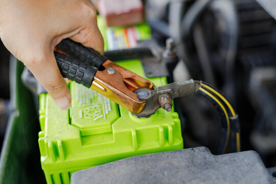 Hand holding jumper cable clamp near car battery