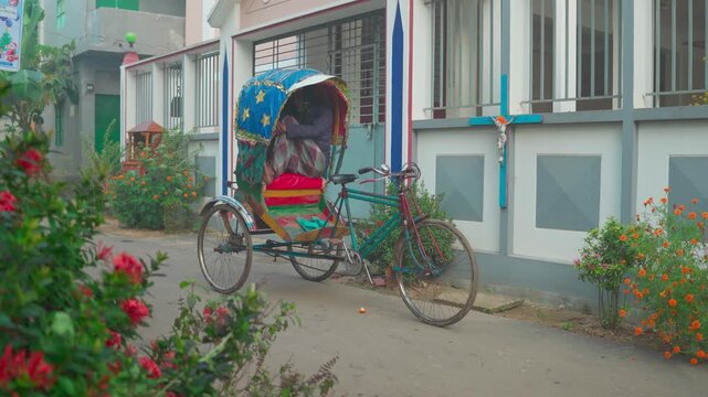 Traditional colorful rickshaw with a puller resting inside on a quiet street.