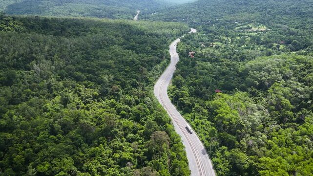 High-angle drone footage of a winding mountain road cutting through dense green forest, capturing natural landscape, scenic travel route, and peaceful countryside environment from above.