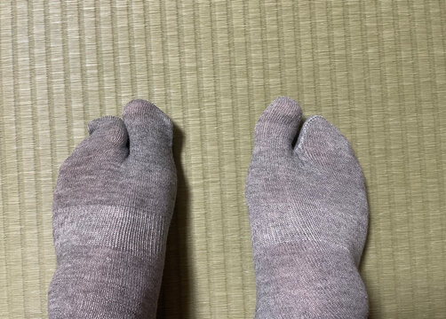 Traditional Japanese tabi split toe socks on two feet resting on a tatami mat