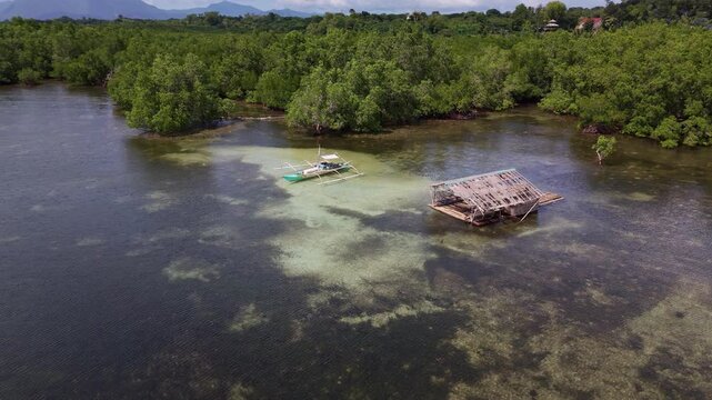 Slow descent drone shot showing traditional bangka outrigger boat and floating bamboo hut among mangrove shallows near Bancao-Bancao in Puerto Princesa on Palawan Philippines