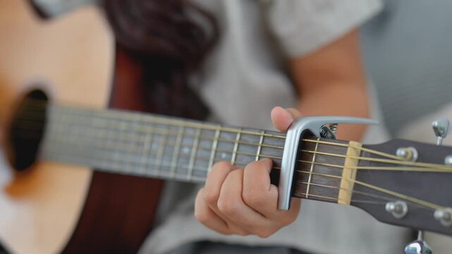 Close-up of a Person Playing Acoustic Guitar with a Capo on the Fretboard, Showcasing Finger Position and Musical Expression in a Cozy Environment