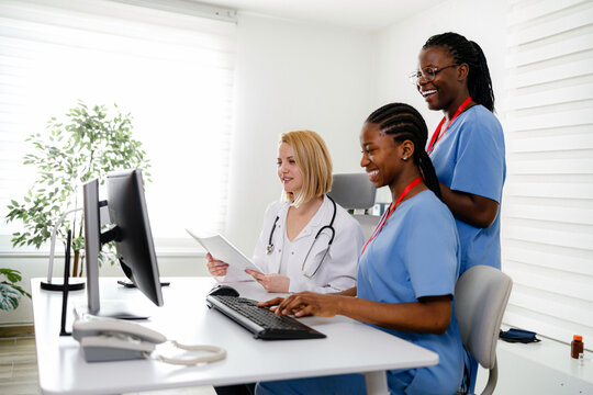 Three healthcare professionals work together at a computer in a bright office setting