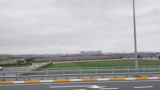 Wide angle tracking shot from a moving car of a modern roadside building and highway infrastructure under a cloudy sky. Clean urban landscape featuring transit and utility structures