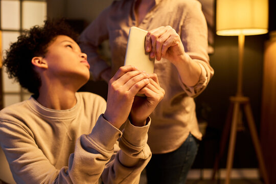 Teenager holding smartphone while parent taking device away during home conflict, illustrating screen time control. Useful for parenting, digital wellbeing, family rules